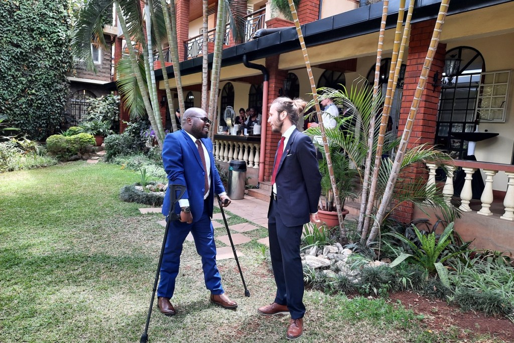 A Finnish and a Kenyan man discussing in a green garden in front of a building