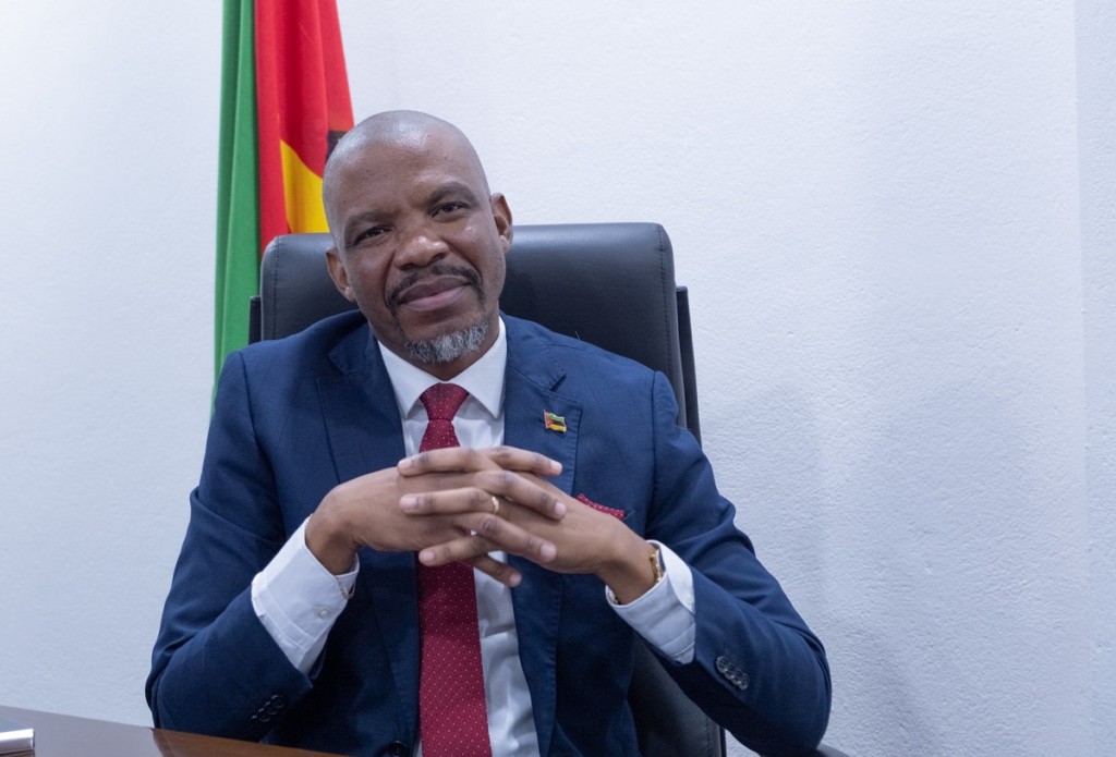 Mies istuu tuolissa ja katsoo kameraan, taustalla Mosambikin lippu