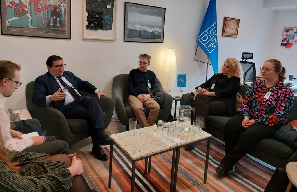 People are sitting on couches and chatting, there is a UNDP flag in the background