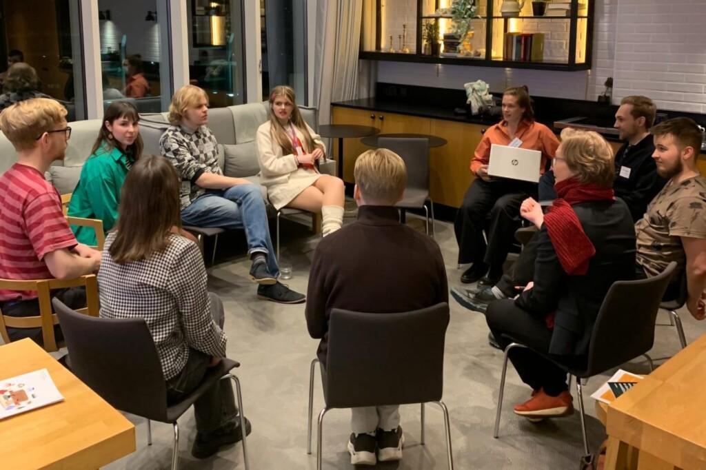 A group of young people sitting in a circle on chairs.