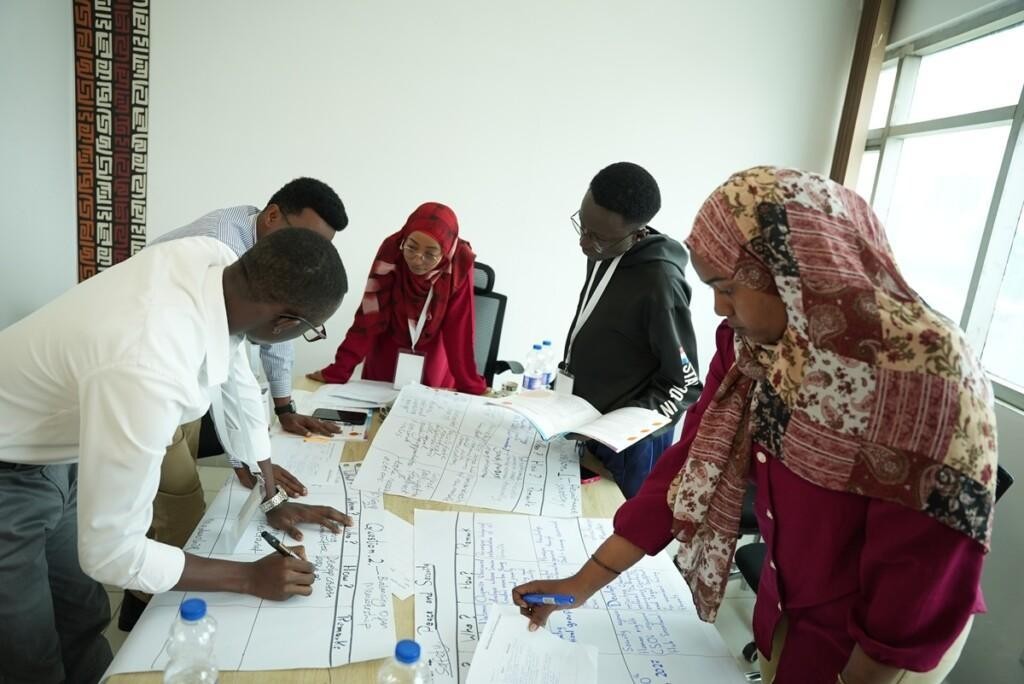 Young people writing on flipcharts around a table.