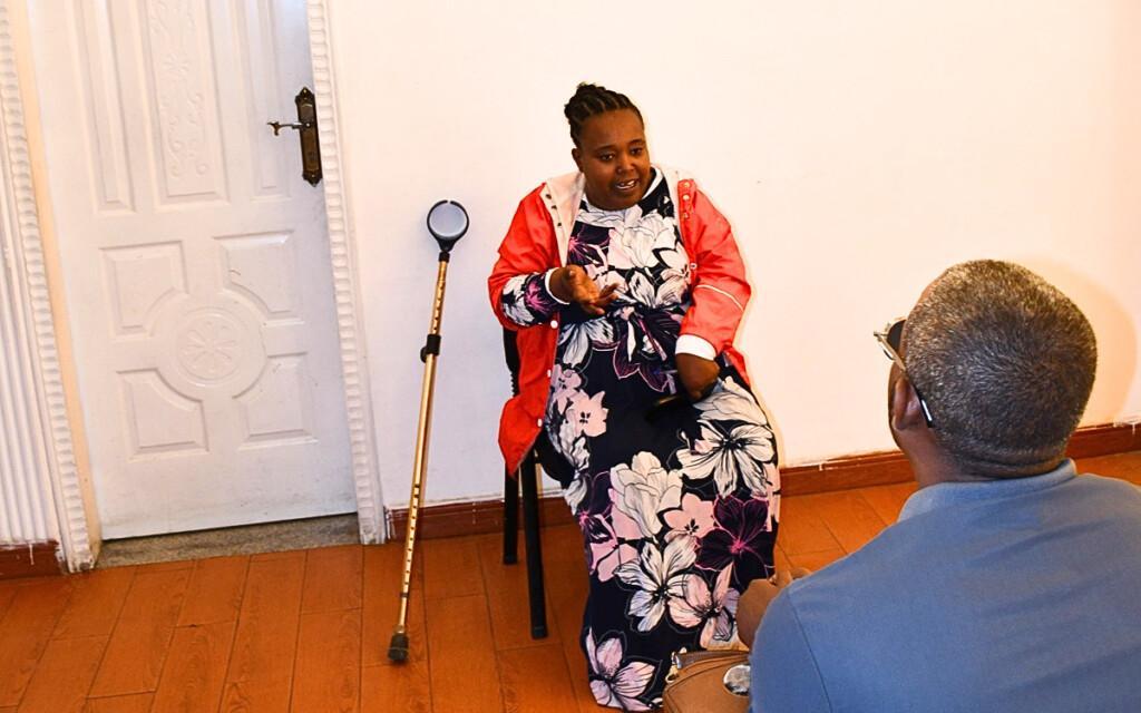 A woman is being interviewed, and next to her, a crutch is leaning on the wall.